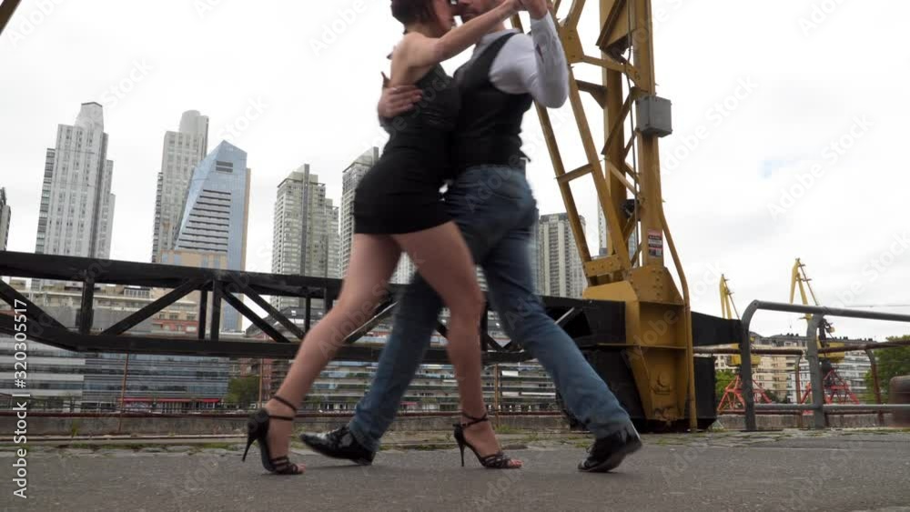 Two skilled dance partners doing a tango routine between cranes with Puerto Madero buildings in background Two skilled dance partners doing a tango routine between cranes with Puerto Madero buildings in background