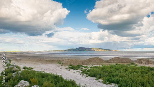 Fototapeta Naklejka Na Ścianę i Meble -  A view of spectacular white fluffy clouds at Dollymount Strand, County Dublin, Ireland. Howth Head peninsula can be seen in the distance.