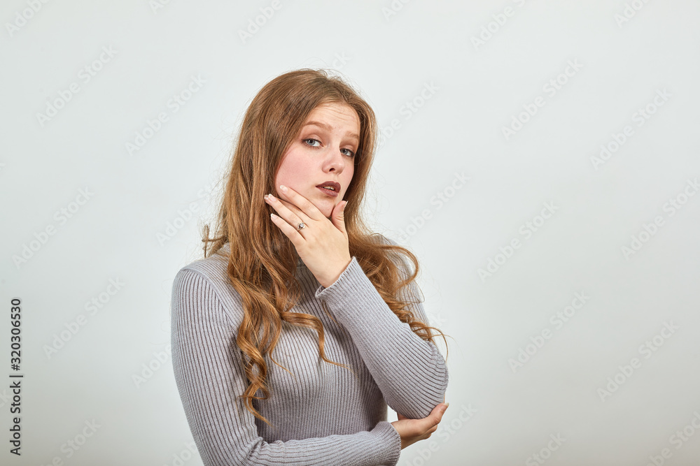 young woman with red hair thinks makes decisions, creates new idea, holding her hand on her chin in gray sweater young woman with red hair thinks makes decisions, creates new idea, holding her hand on her chin in gray sweater