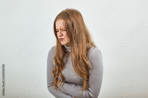 A young red haired woman in gray sweater tilted her body from the pain in stomach because she got bellyache