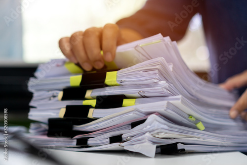 Stacks documents of paper files, Businessman hands working in messy bureaucracy and searching information on office, Accounting budget report file, arranging unfinished of paperwork on busy overwork photo