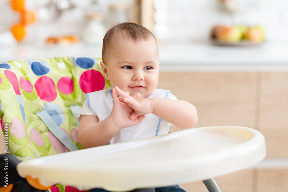Happy baby clapping hands, sitting in high chair in kitchen Happy baby clapping hands, sitting in high chair in kitchen
