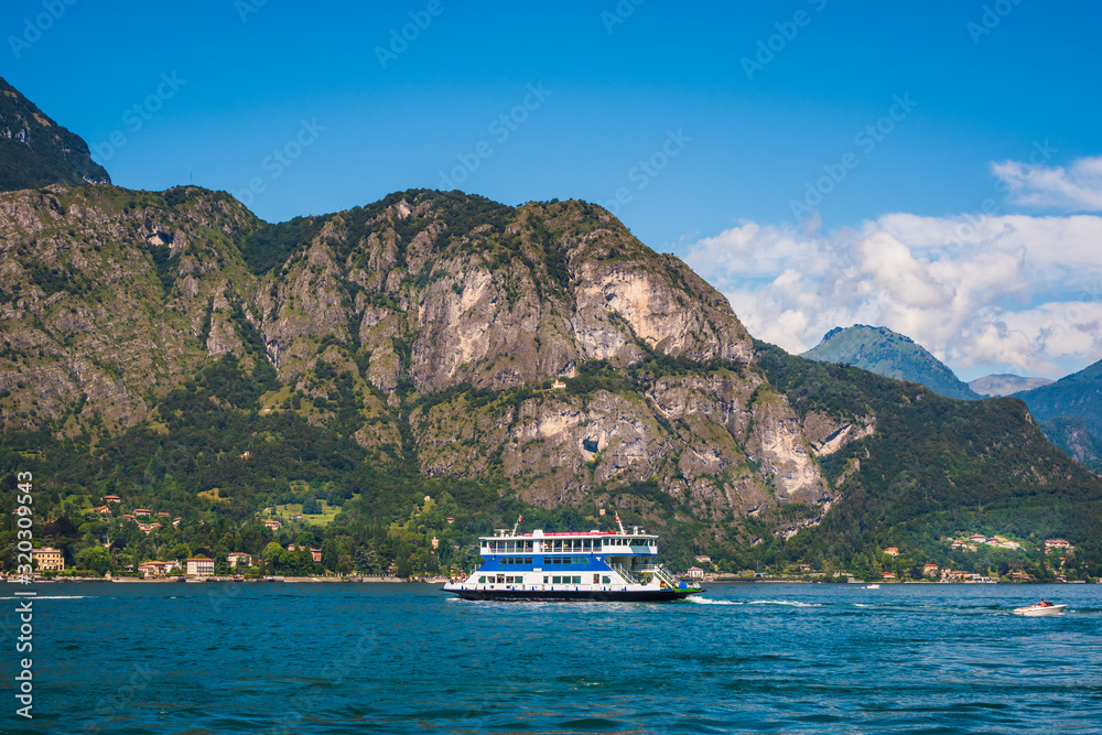 Picturesque summer landscape from Lake Como, ferry boat on the alpine lake, blue sky and high mountain in the background, Province of Como, Italy. Picturesque summer landscape from Lake Como, ferry boat on the alpine lake, blue sky and high mountain in the background, Province of Como, Italy.