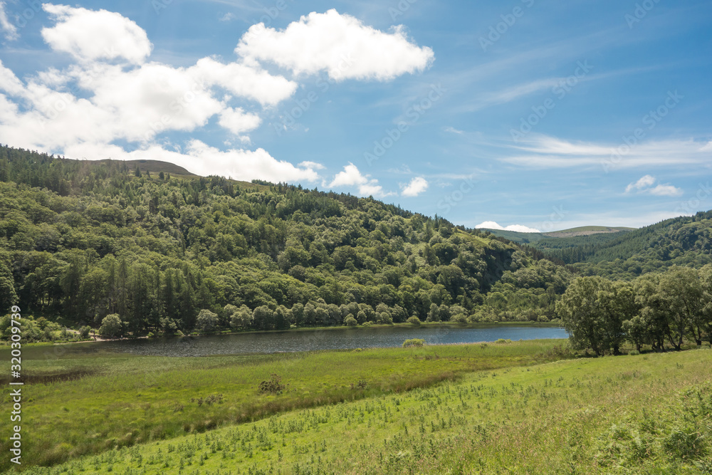 The Lower Lake and hilly woodland on a Summer's day at Glendalough National Park, County Wicklow, Ireland. The Lower Lake and hilly woodland on a Summer's day at Glendalough National Park, County Wicklow, Ireland.