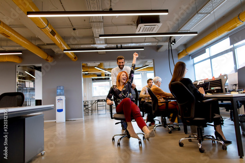 Young business people in smart casual wear having fun while racing on office chairs and smiling