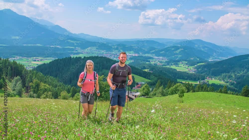 Couple wearing backpacks hiking through lush meadows and mountains on a summer's day. Couple wearing backpacks hiking through lush meadows and mountains on a summer's day.