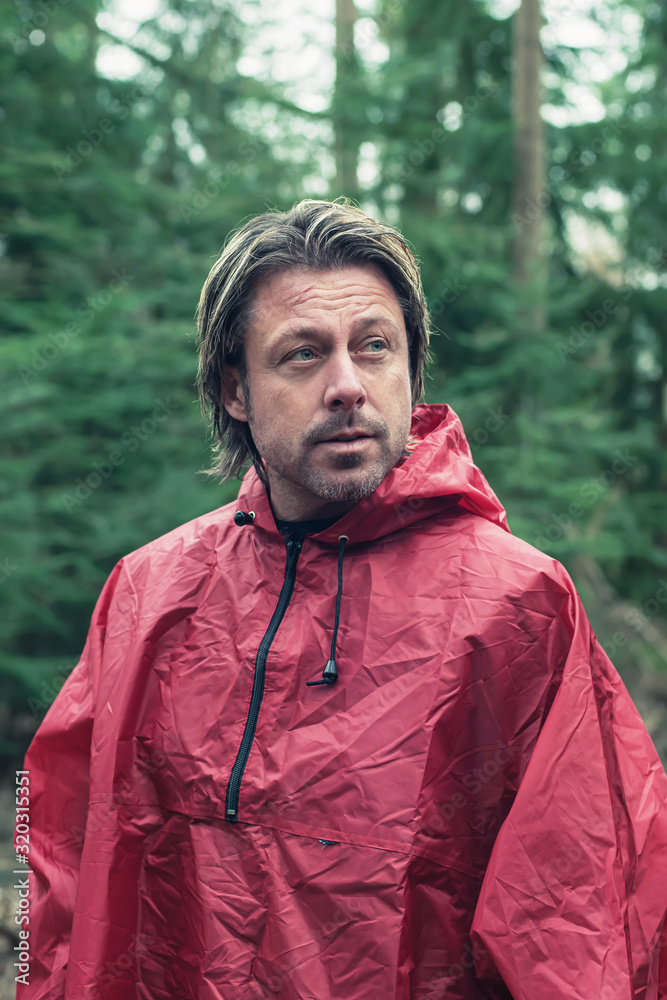 Middle aged man in red raincoat in forest.
