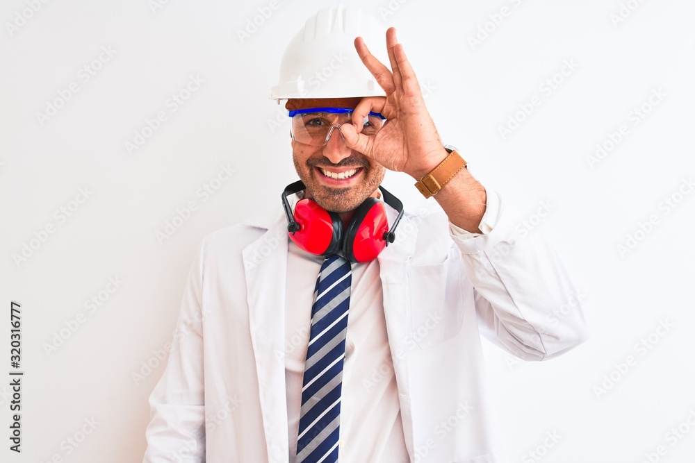Young chemist man wearing security helmet and headphones over isolated background doing ok gesture with hand smiling, eye looking through fingers with happy face. Young chemist man wearing security helmet and headphones over isolated background doing ok gesture with hand smiling, eye looking through fingers with happy face.