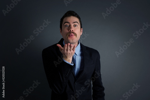 Cute appealing male blows kiss at camera, demonstrates love to girlfriend or says goodbye on distance, isolated over white studio background. Attractive young man shows sympathy to someone.