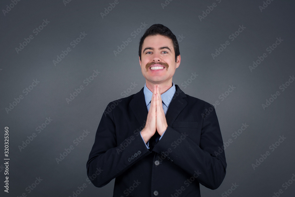 Horizontal portrait of pretty blond man keeps palms together, has pleased expression. Glad attractive male makes request, pleads for mercy. Hopeful young adult.
