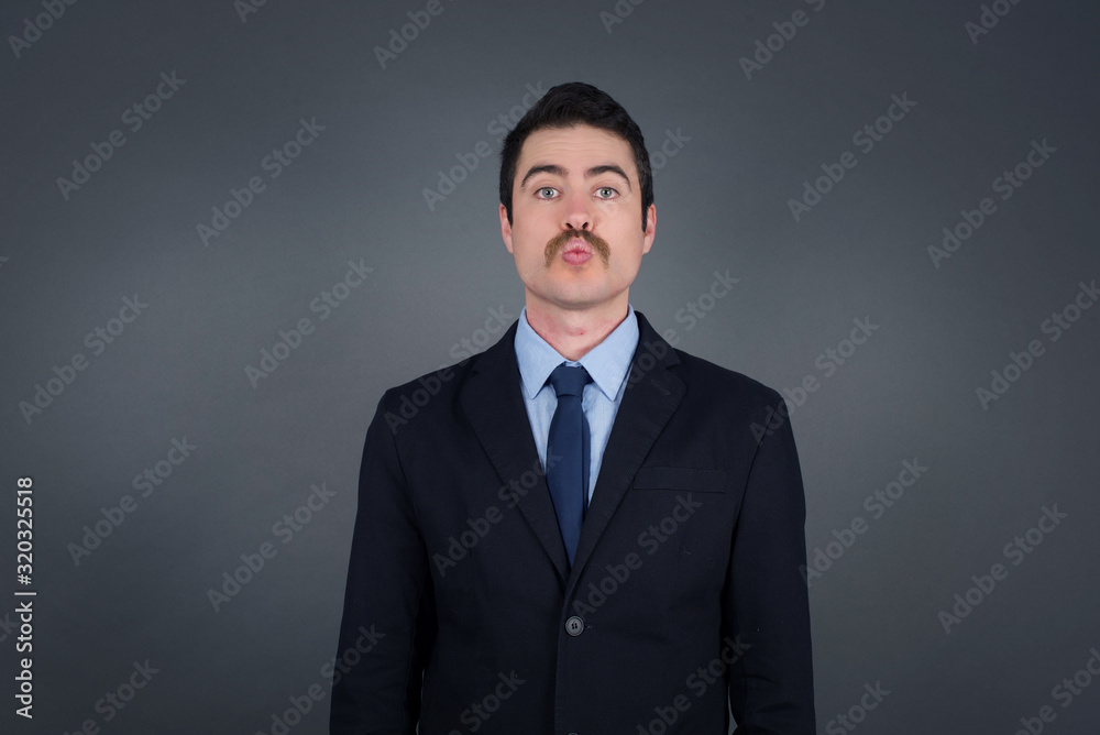 Attractive light haired male rounds lips, wears casual clothes, looks directly into camera, expresses her satisfaction, isolated over gray background. People, body language concept†Attractive light haired male rounds lips, wears casual clothes, looks directly into camera, expresses her satisfaction, isolated over gray background. People, body language conceptâ€