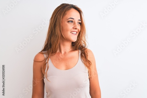 Young redhead woman wearing casual t-shirt stading over white isolated background looking away to side with smile on face, natural expression. Laughing confident.