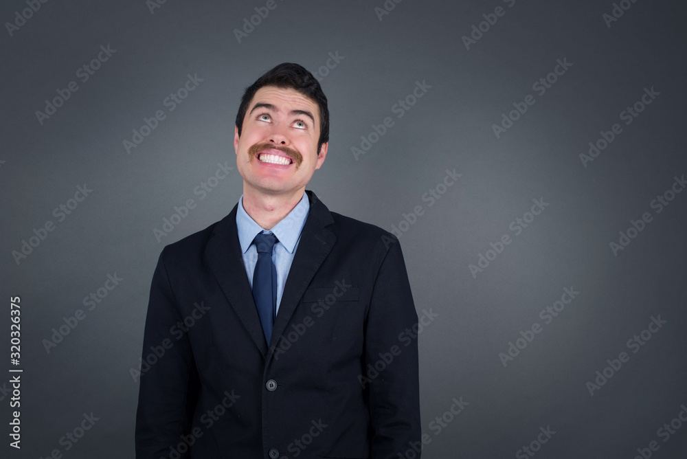 Portrait of mysterious charming blond male looking up with enigmatic smile. Handsome smiling guy looking up standing against gray wall. Portrait of mysterious charming blond male looking up with enigmatic smile. Handsome smiling guy looking up standing against gray wall.