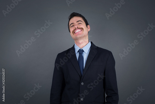 Gorgeous smiling male with broad smile, shows white teeth, wears casual t shirt, stands over gray studio wall rejoices having day off. Man standing indoors. © Jihan