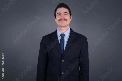 Close up studio shot of handsome young businessman model with curly dark hair looking at camera with charming cute smile while posing against white blank copy space wall for your content