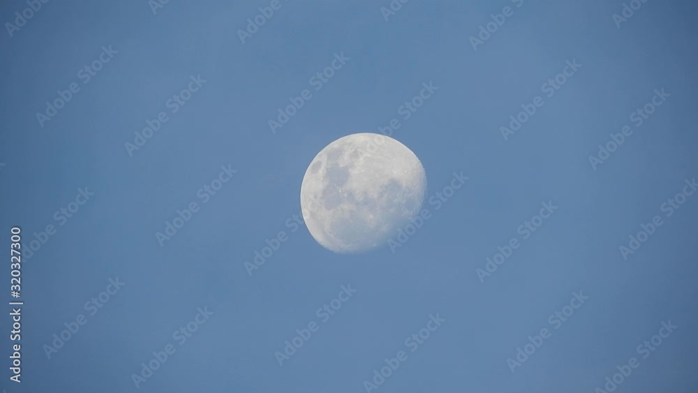 Twilight near full moon moving across the late afternoon sky before sunset with clouds moving past, clear visible crater detail Twilight near full moon moving across the late afternoon sky before sunset with clouds moving past, clear visible crater detail