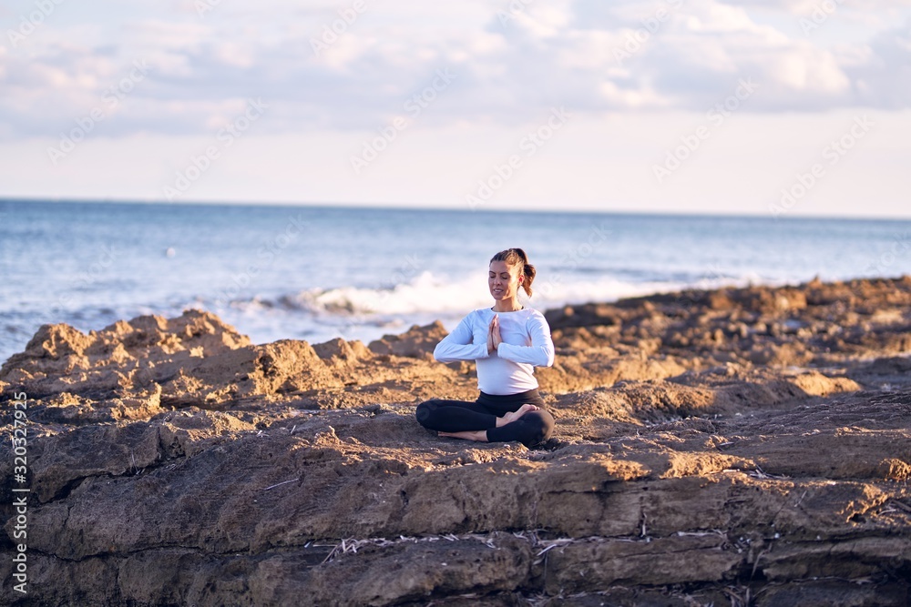 Young beautiful sportwoman smiling happy practicing yoga. Coach with smile on face teaching prayer pose at the beach