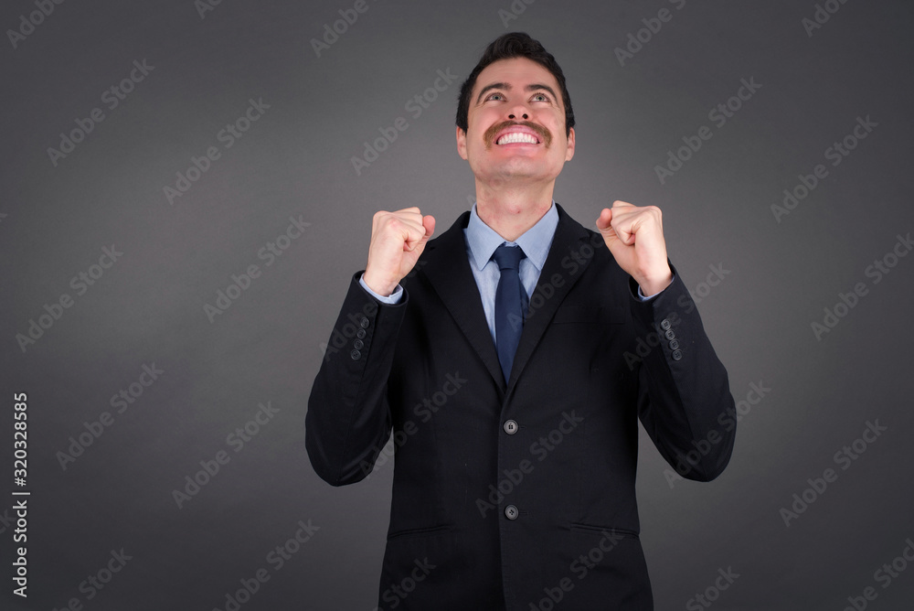 Excited Handsome businessman raising his fists with great happiness having good mood after winning game. Young champion having success being glad to achieve his goals. Victory and triumph concept.