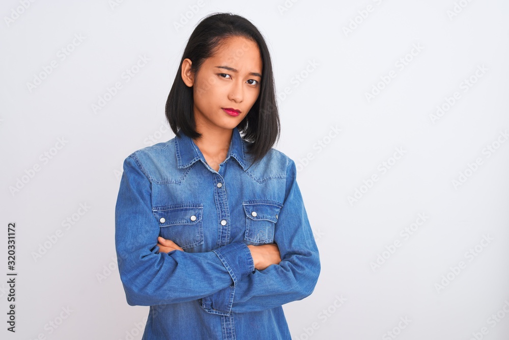 Young beautiful chinese woman wearing denim shirt standing over isolated white background skeptic and nervous, disapproving expression on face with crossed arms. Negative person. Young beautiful chinese woman wearing denim shirt standing over isolated white background skeptic and nervous, disapproving expression on face with crossed arms. Negative person.