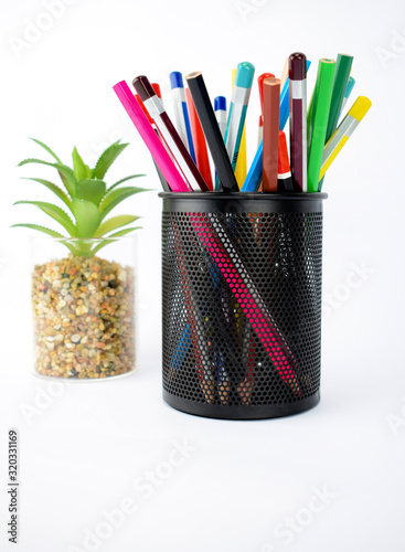 Side view of a jar full of different colored pencils and crayons beside a green tree