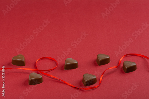 Top view on red ribbon around a chocolate hearts isolated on a red background. Valentine's day concept. 14 february love day