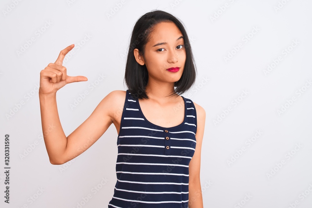 Young chinese woman wearing striped t-shirt standing over isolated white background smiling and confident gesturing with hand doing small size sign with fingers looking and the camera. Measure Young chinese woman wearing striped t-shirt standing over isolated white background smiling and confident gesturing with hand doing small size sign with fingers looking and the camera. Measure