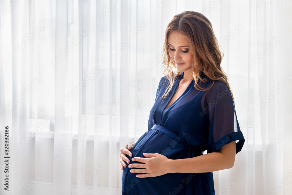 Pregnant woman sits front the window and touching her belly. Pregnant woman sits front the window and touching her belly.
