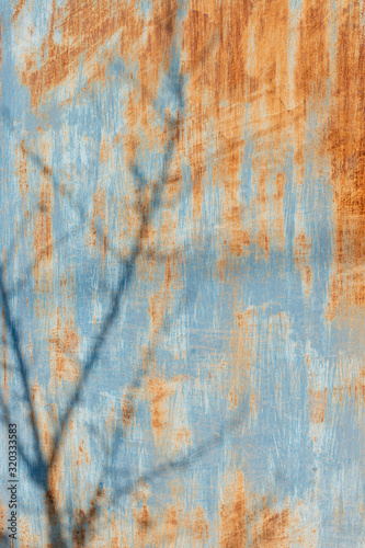 rusty metal surface painted in blue color with a shadow on the tree branches. vertical image.