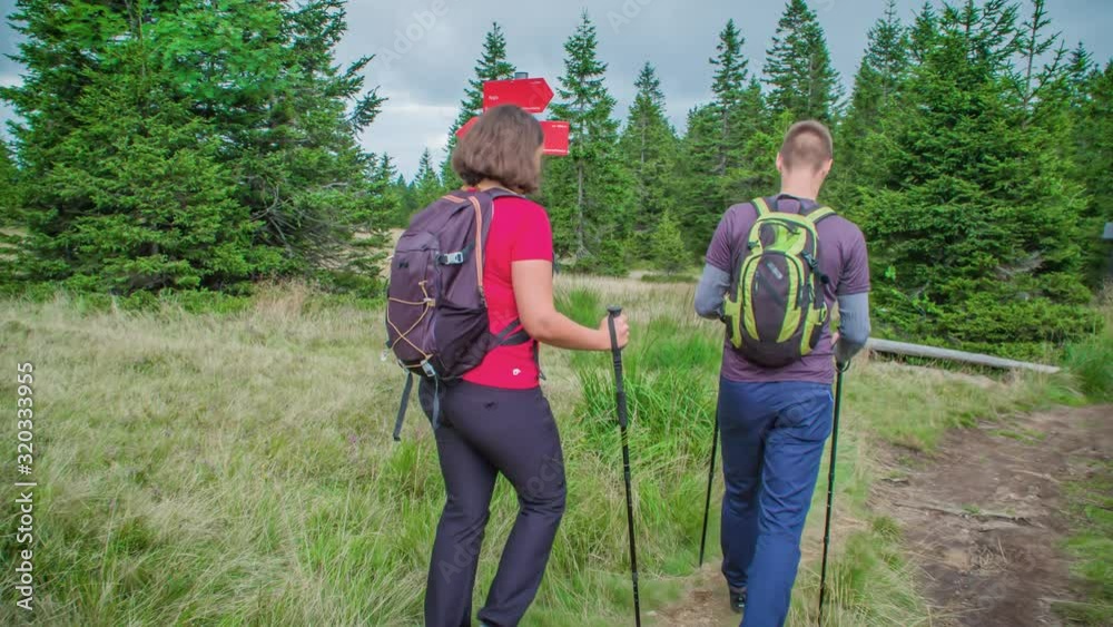 Hikers reading directional sign in grassland as they walk into wooded area. Hikers reading directional sign in grassland as they walk into wooded area.