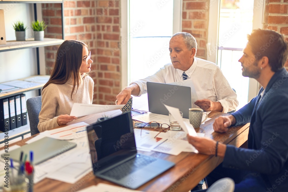 Group of business workers working together. Sitting on desk using laptop reading documents at the office Group of business workers working together. Sitting on desk using laptop reading documents at the office
