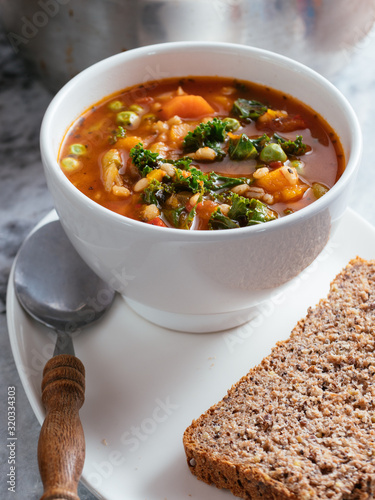 Home made Italian winter minestrone soup with winter squash, carrots, kale, green beans, peas, tomatoes and barley