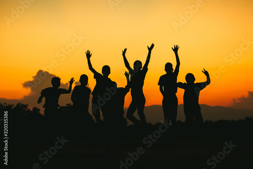 Silhouette group of happy jumping kids under the yellow sunset sky. Concept for happiness and freedom life of young people..