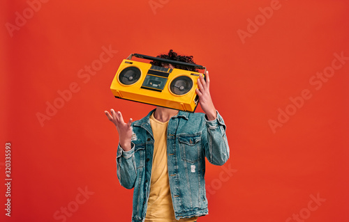 Studio shot of man catching or throwing retro music player, which hiding his face. Isolated on red background photo