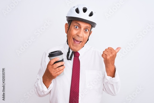 Senior businessman wearing bike helmet drinking coffee over isolated white background pointing and showing with thumb up to the side with happy face smiling