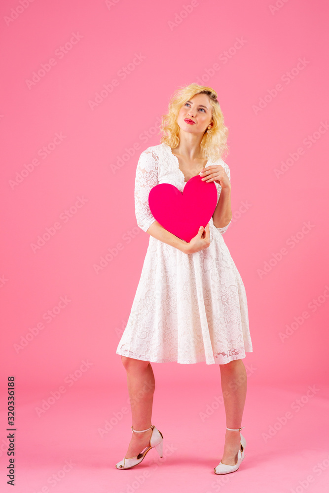 Full body studio portrait of a young casual woman holding pink heart and looking up Full body studio portrait of a young casual woman holding pink heart and looking up
