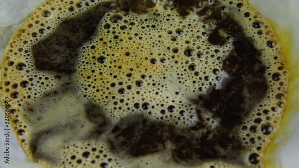 Slow motion close up of water been poured from a kettle on to black coffee within a white filter Slow motion close up of water been poured from a kettle on to black coffee within a white filter
