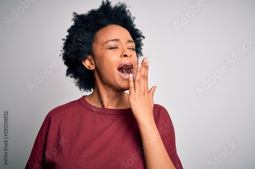 Young beautiful African American afro woman with curly hair wearing casual t-shirt standing bored yawning tired covering mouth with hand. Restless and sleepiness.