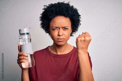 Young African American afro woman with curly hair drinking bottle of water for refreshment annoyed and frustrated shouting with anger, crazy and yelling with raised hand, anger concept