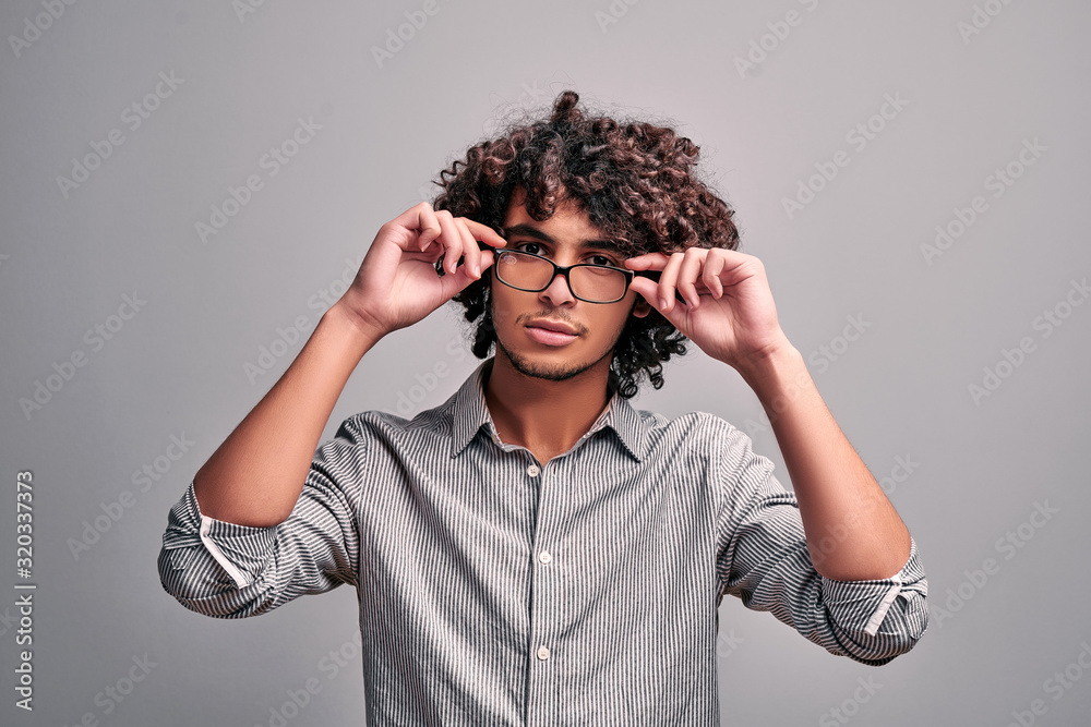 Image on isolated background of young handsome eastern man holding hands on his eyeglasses. Image on isolated background of young handsome eastern man holding hands on his eyeglasses.