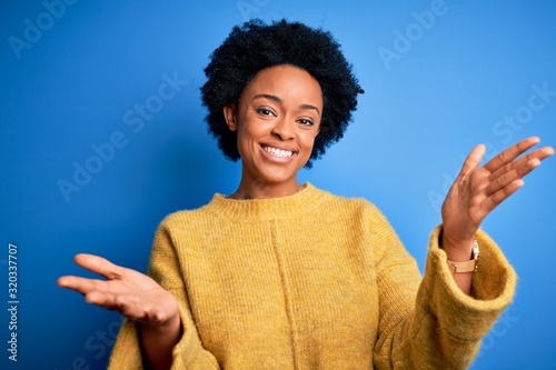 Quadro su tela Young beautiful African American afro woman with curly hair wearing yellow casual sweater smiling cheerful offering hands giving assistance and acceptance