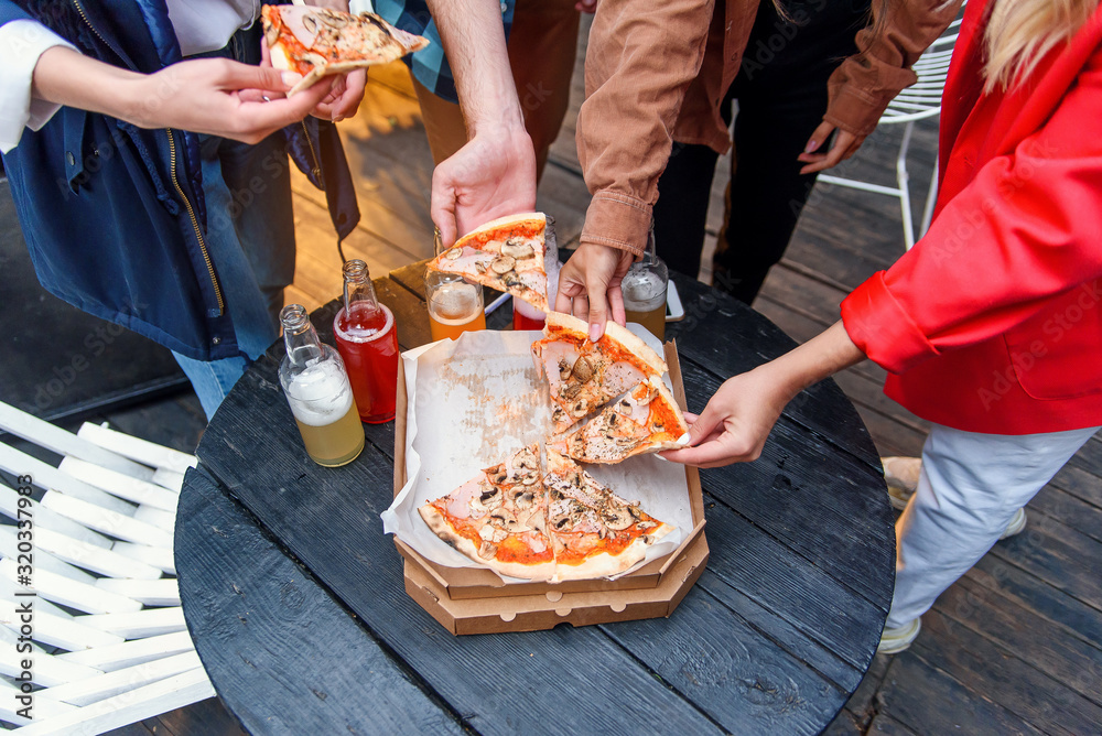Group of young friends hands taking slices of pizza from the box.