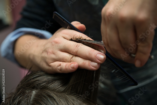 Hands of professional hair stylist cutting client shot hair.