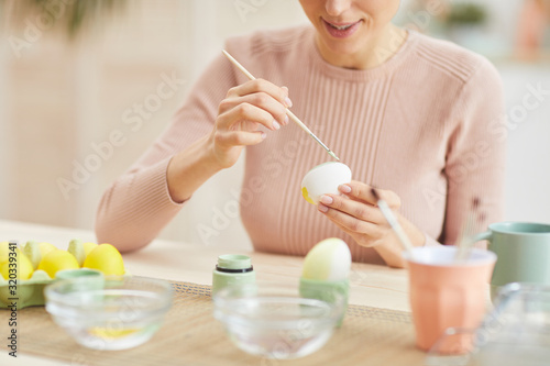 Cropped portrait of smiling young woman painting Easter eggs while sitting at table in cozy kitchen interior  copy space