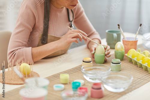 Cropped portrait of unrecognizable young woman painting eggs in pastel colors for Easter while sitting at table in kitchen or art studio  copy space