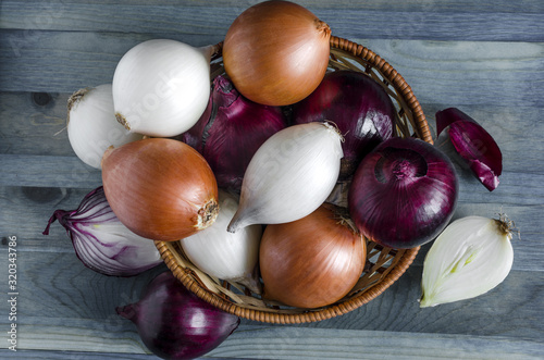 large bulbs of yellow  red and white onions in a basket on a blue background top view