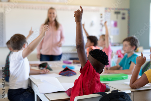 Group of schoolchildren raising their hands in an elementary school classroom