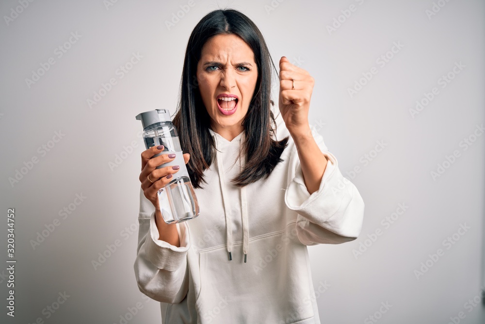 Young brunette sporty woman with blue eyes holding water bottle over white background annoyed and frustrated shouting with anger, crazy and yelling with raised hand, anger concept Young brunette sporty woman with blue eyes holding water bottle over white background annoyed and frustrated shouting with anger, crazy and yelling with raised hand, anger concept