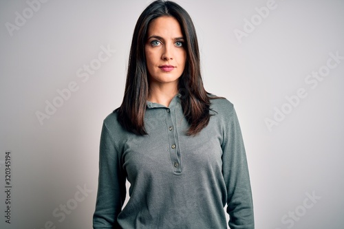 Young brunette woman with blue eyes wearing casual green sweater over white background with serious expression on face. Simple and natural looking at the camera.