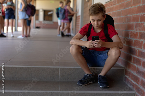 Schoolboy sitting on a step in the schoolyard at elementary school using a smartphone