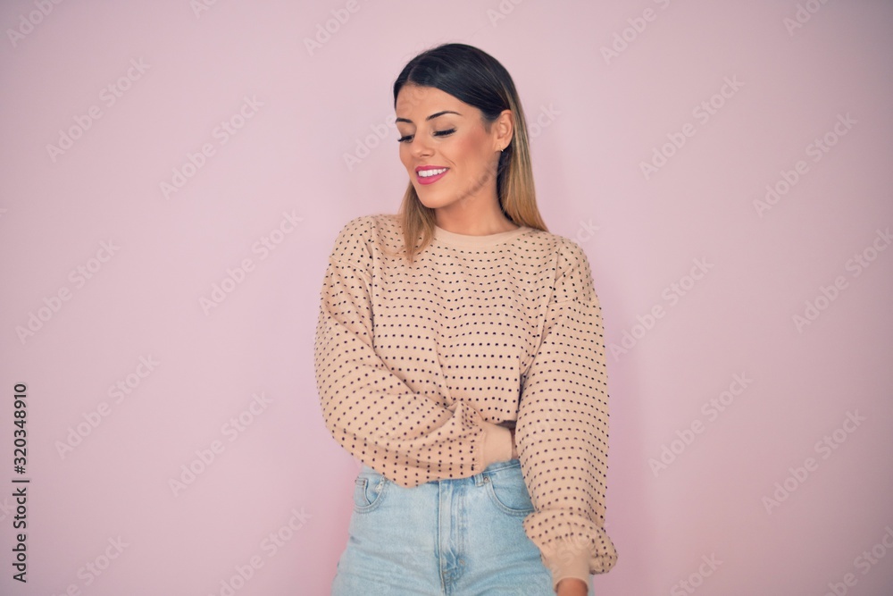 Fototapeta premium Young beautiful woman wearing fashionable clothes smiling happy and confident. Standing with smile on face over isolated pink background